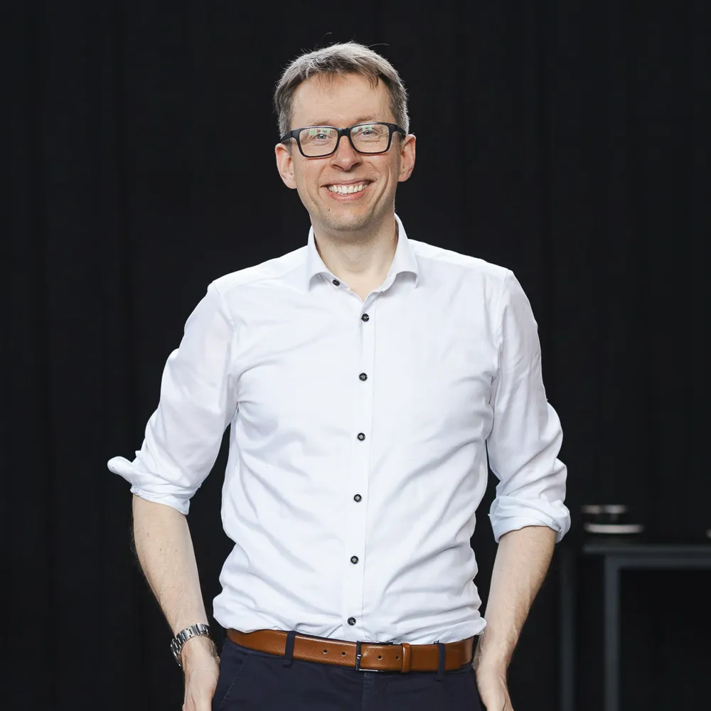 Daniel Schwenger steht mit den Händen in den Taschen und lächelt